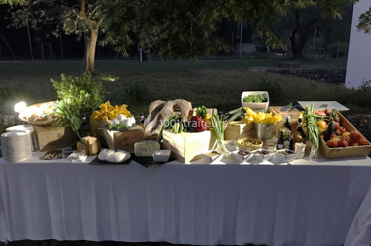 Traiteur Jerome Ravel Traiteur Mouans-Sartoux #1 Table de buffet en extérieur avec légumes frais, fromages, pains et condiments, éclairée sous des arbres.