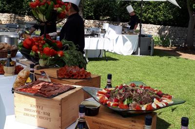 Traiteur Jerome Ravel Traiteur Mouans-Sartoux #4 Buffet en plein air avec charcuterie, fruits, et bouteilles de vin, sous des parasols dans un jardin verdoyant.