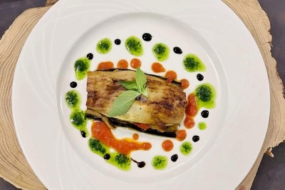 Traiteur Traiteur Lallemand Montblanc #2 Assiette garnie d'un plat à base d'aubergine grillée, décorée de sauces colorées et d'une feuille de basilic.