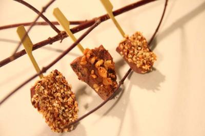 Trois bouchées chocolatées enrobées de noisettes concassées, présentées sur des branches en bois.