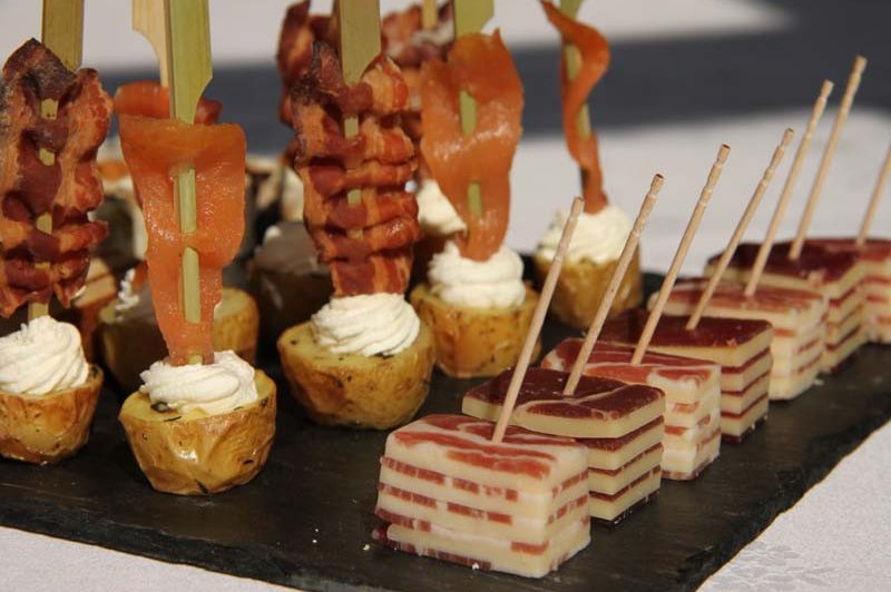 Plateau d'amuse-bouches comprenant brochettes de bacon, pommes de terre garnies et cubes de fromage en couches.