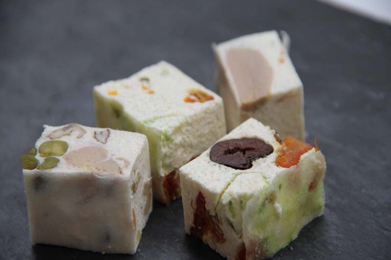 Quatre morceaux de nougat aux fruits secs et confits, disposés sur une surface sombre.