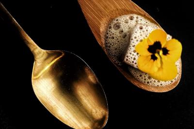Traiteur Jacques Lafargue Traiteur Chaponost #1 Cuillère dorée à côté d'une cuillère en bois contenant une mousse, un cube et une fleur jaune.