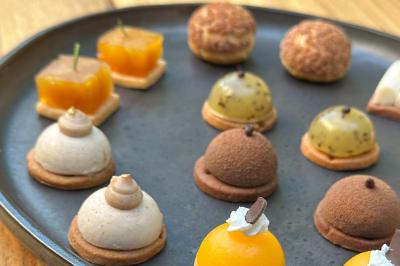 Traiteur Arômes et Sens Sèvres #5 Assortiment de mini-pâtisseries variées disposées sur une assiette noire, présentées sur une table en bois.
