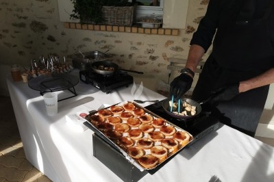 Un cuisinier prépare des bouchées dans une poêle à côté de tartelettes disposées sur une table blanche.
