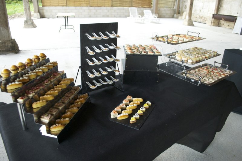 Buffet de petits fours variés disposés sur des présentoirs noirs dans un espace ouvert et lumineux.