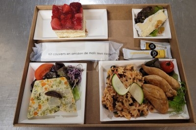 Plateau-repas composé de légumes, pâtes, fromage, dessert aux fraises et couverts emballés sur une table.