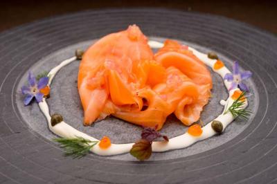 Tranches de saumon fumé disposées sur une assiette avec crème, câpres, œufs de poisson et décorations florales.