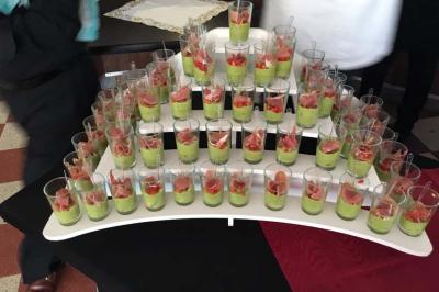 Présentoir avec plusieurs verrines contenant une préparation verte garnie de morceaux de jambon et de légumes.