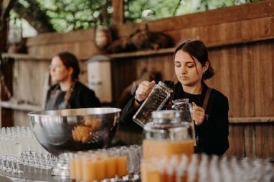 Traiteur Stéphane Portier Traiteur Le Plessis-Macé #5 Une femme verse une boisson dans un verre sur un comptoir avec des jus et des verres alignés, en arrière-plan une autre…
