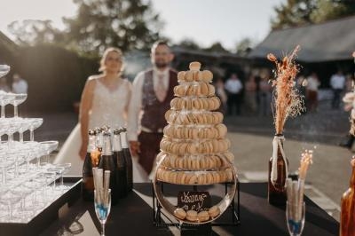 Traiteur Stéphane Portier Traiteur Le Plessis-Macé #2 Tour de macarons sur une table de réception en extérieur, avec un couple en arrière-plan et des bouteilles de champagne.
