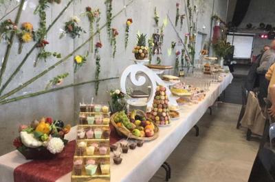 Traiteur L'Etang Moderne Saint-Philbert-de-Bouaine #1 Table garnie de desserts, fruits et boissons dans une salle décorée de fleurs fixées sur un mur en béton.
