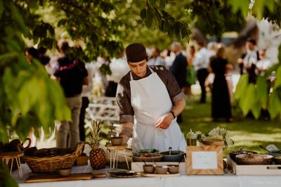 Traiteur Au Bois du Bon Sejour Aubeterre #3 Un cuisinier prépare un buffet en plein air sous des arbres, avec des plats et des fruits disposés sur une table.