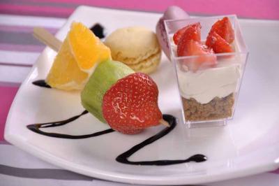 Assortiment de desserts comprenant brochette de fruits, macaron, verrine aux fraises et coulis décoratif.