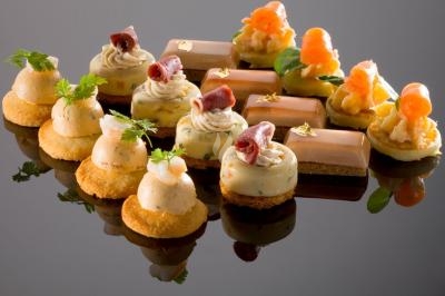 Assortiment de bouchées apéritives élégantes, comprenant mousse, saumon fumé, jambon et décorations raffinées.
