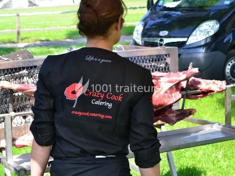 Traiteur Crazy Cook Catering Gottesheim #1 Une femme de dos portant une veste de traiteur devant une carcasse de viande sur un grill en plein air.