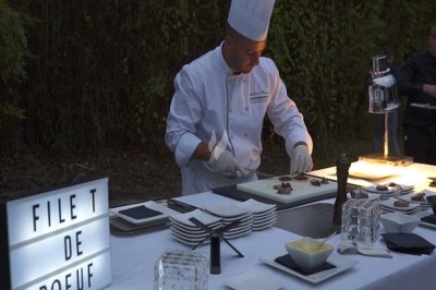 Traiteur Lapierre Traiteur Saint-Denis #2 Un chef en tenue blanche découpe du filet de bœuf sur une table dressée en extérieur, éclairée par une lampe.