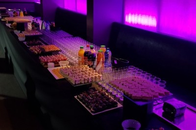 Traiteur Lapierre Traiteur Saint-Denis #4 Buffet avec verrines, amuse-bouches, boissons et desserts disposés sur une longue table éclairée par une lumière violette.