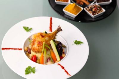 Traiteur Le Maydane Avs Clamart #5 Plat de couscous garni de légumes, pois chiches et cuisse de poulet, avec épices en arrière-plan.