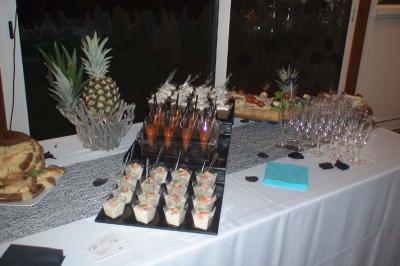 Traiteur Spirale Gourmande Unverre #3 Buffet avec verrines, brochettes, ananas décoratif, verres vides et nappe blanche dans un cadre intérieur.