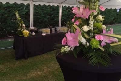 Traiteur Spirale Gourmande Unverre #4 Arrangement floral avec des lys roses sur une table haute, devant un buffet sous une tente blanche en extérieur.