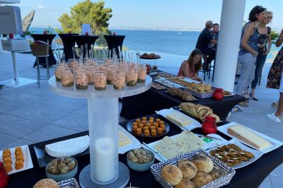 Traiteur Traiteur Calabria - Le Domus Martigues #3 Buffet en extérieur avec vue sur la mer, comprenant pains, viennoiseries, fromages et verrines disposés sur des tables.