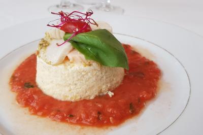 Plat de flan salé garni de basilic, tomate cerise et pousses, entouré d'une sauce tomate sur une assiette blanche.
