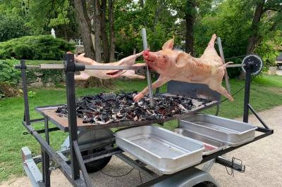 Traiteur Agen Events Agen #4 Cochon entier en cours de cuisson sur une broche rotative au-dessus de braises, dans un cadre extérieur verdoyant.