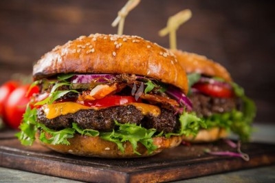 Traiteur L'Atelier de Fred La Chapelle-d'Armentières #4 Deux hamburgers garnis de salade, tomates, oignons rouges, fromage fondu et bacon, servis sur une planche en bois.