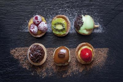 Assortiment de mini-tartelettes garnies de fruits, chocolat et crème, disposées sur une ardoise saupoudrée de cacao.