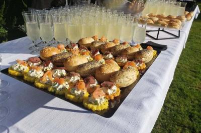 Plateau de mini-sandwichs garnis et verres de boisson claire disposés sur une table blanche en extérieur.