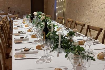 Traiteur Les Trois Sens Saint-Jean-d'Illac #5 Table de réception décorée avec des fleurs blanches et vertes, bougies et vaisselle élégante dans une salle en pierre.