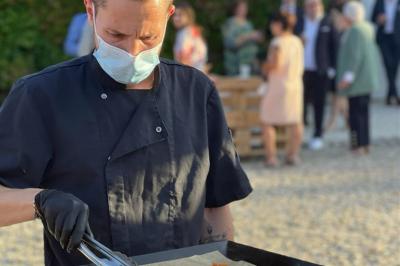 Traiteur Les Trois Sens Saint-Jean-d'Illac #4 Un cuisinier masqué prépare des aliments sur une plancha lors d'un événement en extérieur.