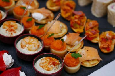 Assortiment de bouchées apéritives comprenant crevettes, saumon, légumes et roulés sur un plateau noir.