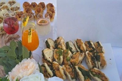 Plateau de mini-sandwichs garnis, accompagnés de cocktails colorés et de bouchées apéritives sur une table décorée.