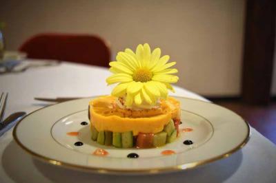 Dessert décoratif avec une fleur jaune sur une base de mousse orange et morceaux d'avocat, présenté sur une assiette.