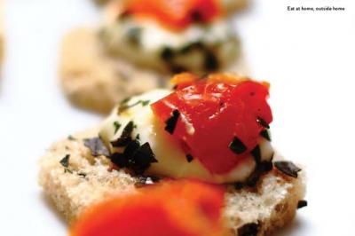 Tranches de pain garnies de fromage fondu, tomates et herbes, présentées en gros plan sur une table.