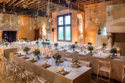 Salle de réception décorée avec des tables alignées, nappes blanches, chaises pliantes et ornements suspendus.