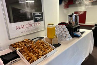 Table avec viennoiseries, jus d'orange, tasses empilées et cafetières, dans un espace intérieur.