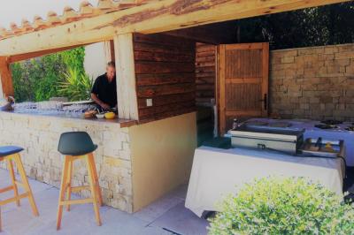 Traiteur Lou Pignatoun Grasse #5 Homme préparant des plats dans une cuisine extérieure en bois et pierre, avec un comptoir et des tables aménagées.