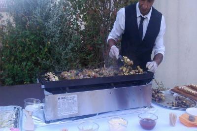 Un serveur en tenue formelle prépare des brochettes sur un gril lors d'un buffet en extérieur.