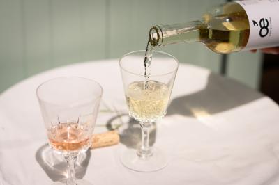 Traiteur Les Vins Oé Lyon 9 #4 Une bouteille de vin blanc est versée dans un verre sur une table blanche, à côté d'un verre de rosé et d'un bouchon.