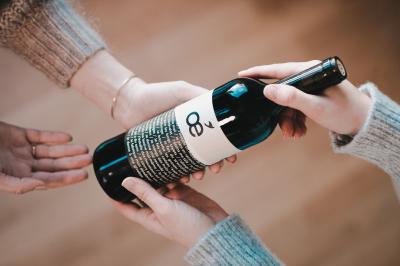 Traiteur Les Vins Oé Lyon 9 #5 Deux mains tendent une bouteille de vin à une troisième main dans un intérieur lumineux.
