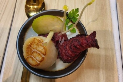 Assiette de dégustation avec une noix de Saint-Jacques, une tranche de betterave, une pomme verte et une herbe décorative.