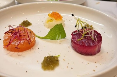 Assiette gastronomique avec saumon, betterave, œufs de poisson et garnitures délicates sur une nappe blanche.