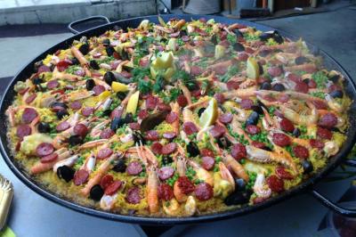 Grande poêle de paella garnie de fruits de mer, chorizo, légumes et quartiers de citron, décorée de persil.