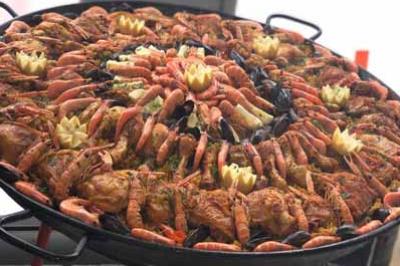 Grande poêle de paella garnie de fruits de mer, poulet, moules et décorations en citron, posée sur un trépied.