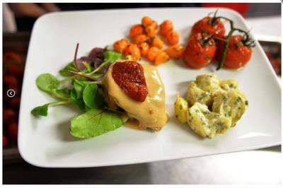 Assiette garnie de légumes grillés, salade verte, viande avec sauce et tomate séchée, accompagnée de pommes de terre.