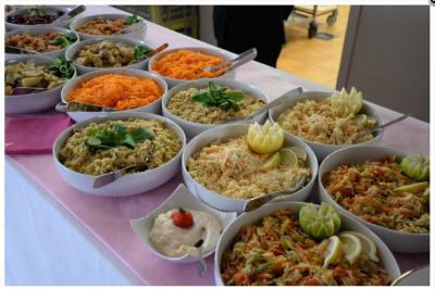 Buffet de salades variées avec carottes râpées, taboulé, légumes, et sauce, présenté dans des bols sur une nappe rose.