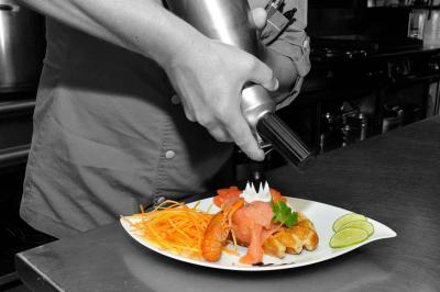 Traiteur Auberge de La Herse Bonneval #4 Un chef décore un plat de saumon, crevettes et légumes avec une mousse à l'aide d'un siphon en cuisine professionnelle.
